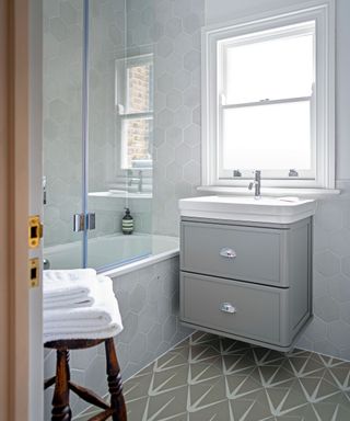 grey bathroom with bathtub, under-sink storage and patterned tiles