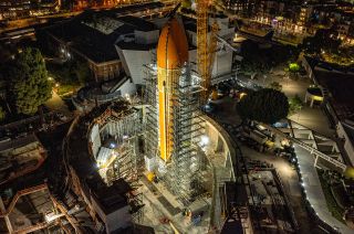 a large orange cylindrical tank stands at night, surrounded by metallic scaffolding.