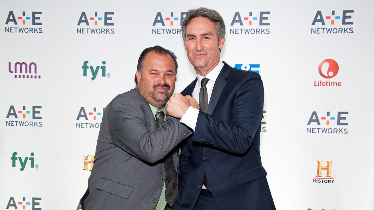 Frank Fritz in a grey suit and Mike Wolfe in a darker suit on an A&amp;E red carpet