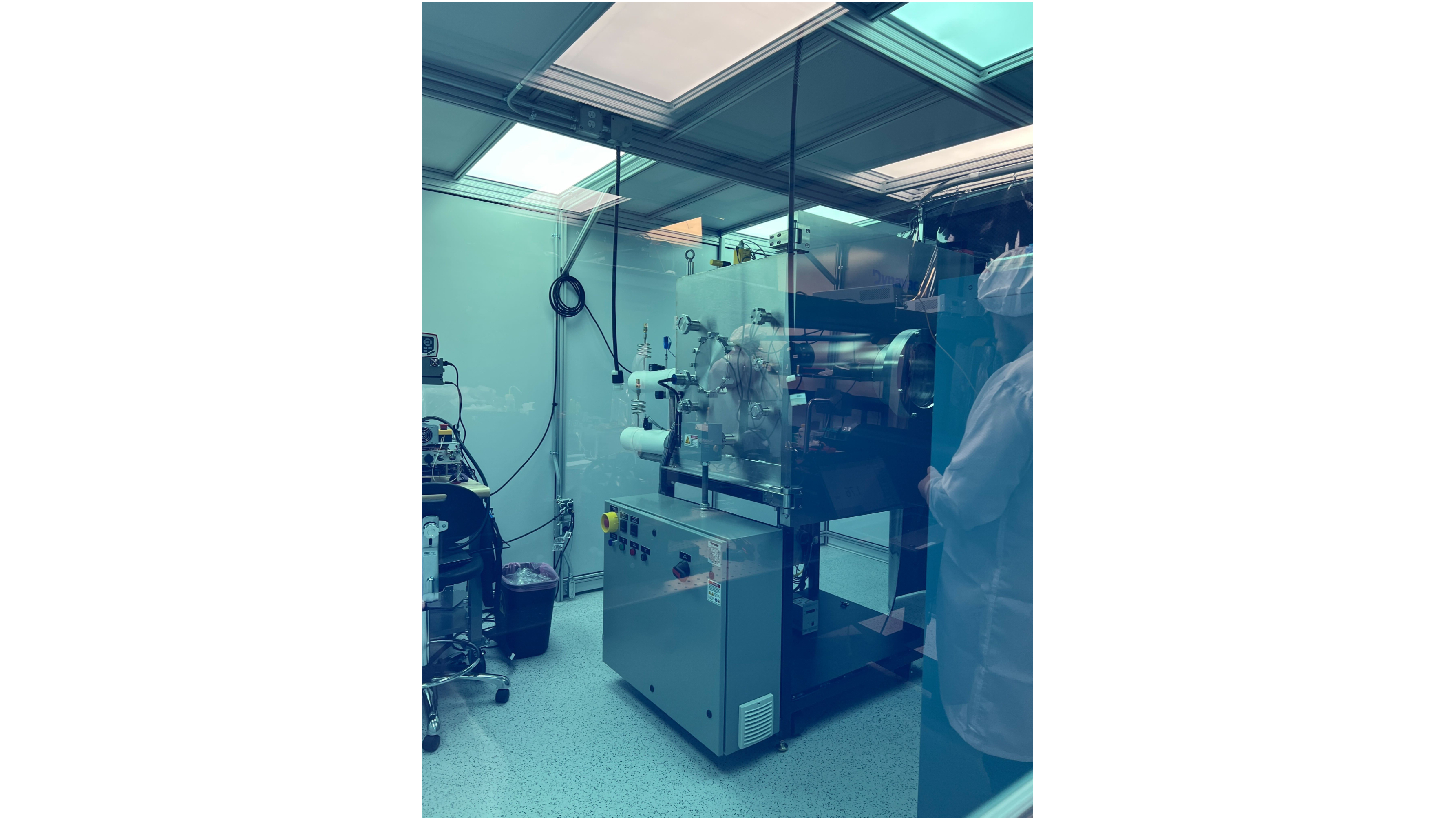 photo of a scientific laboratory, with equipment in a glass case in the center of the frame and a technician wearing a white coat and white hat on the right-hand side