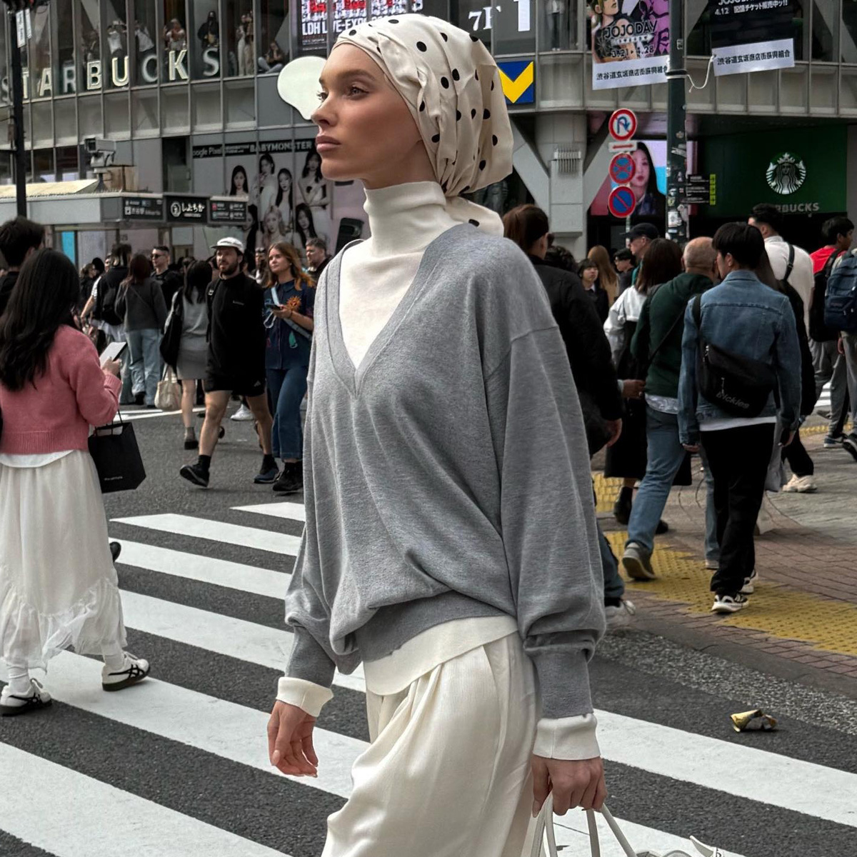 Elsa wears a gray sweater, turtleneck, ivory silk pants, and a polka dot scarf.