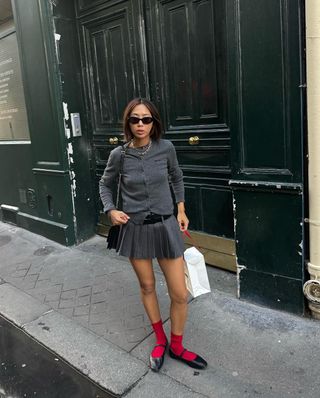 @aimeesong wearing a grey pleated mini skirt with a cardigan