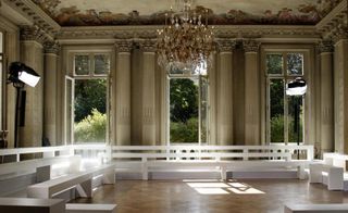 The Hôtel Salomon de Rothschild interior setup for the Martin Margiela show white seating, French doors & grand chandeliers hung under a classically painted ceiling