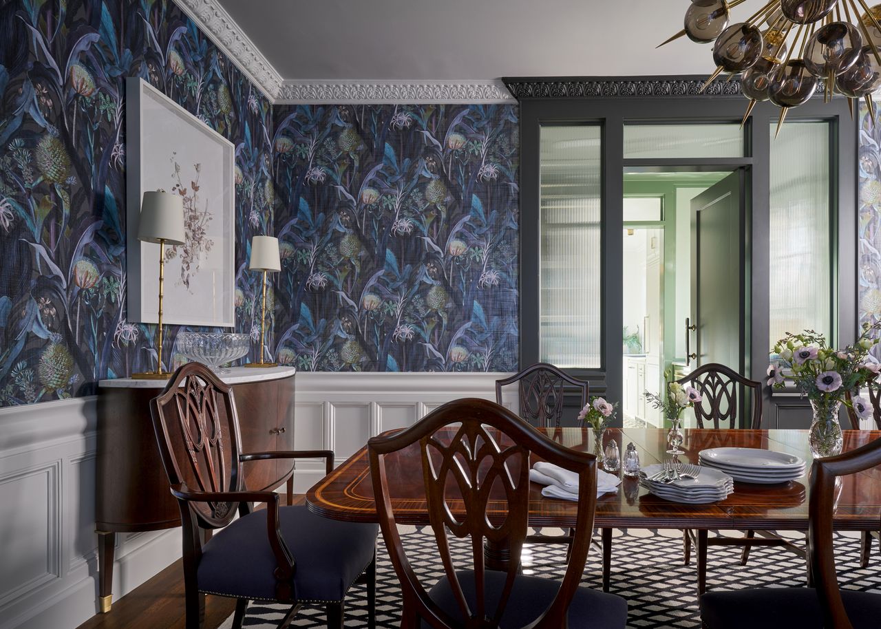 A dining room with a blue patterned wallpaper, and wooden furniture and door frames in grey