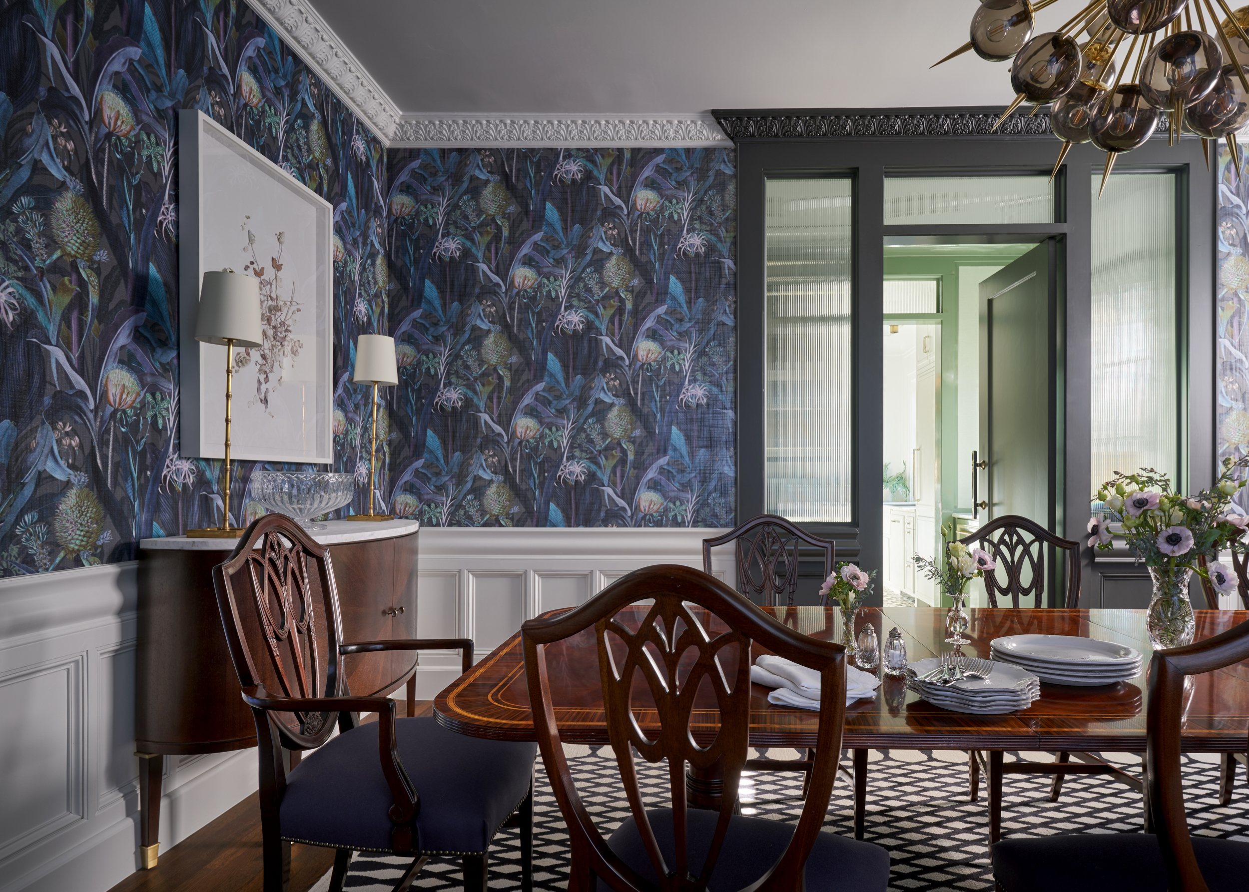 A dining room with a blue patterned wallpaper, and wooden furniture and door frames in grey