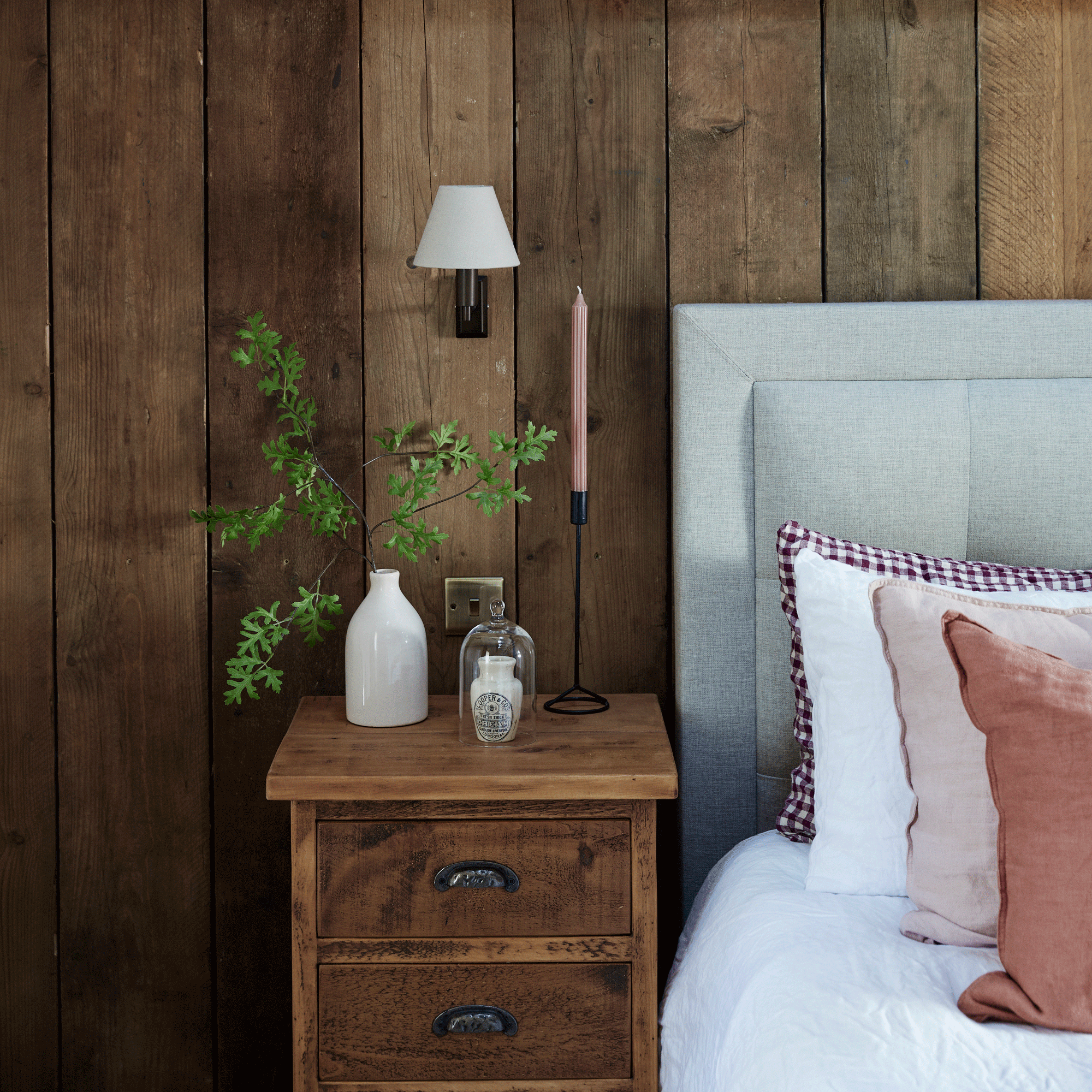 a bedroom with wood cladding on the walls with a matching bedside table beside a bed and a wall light