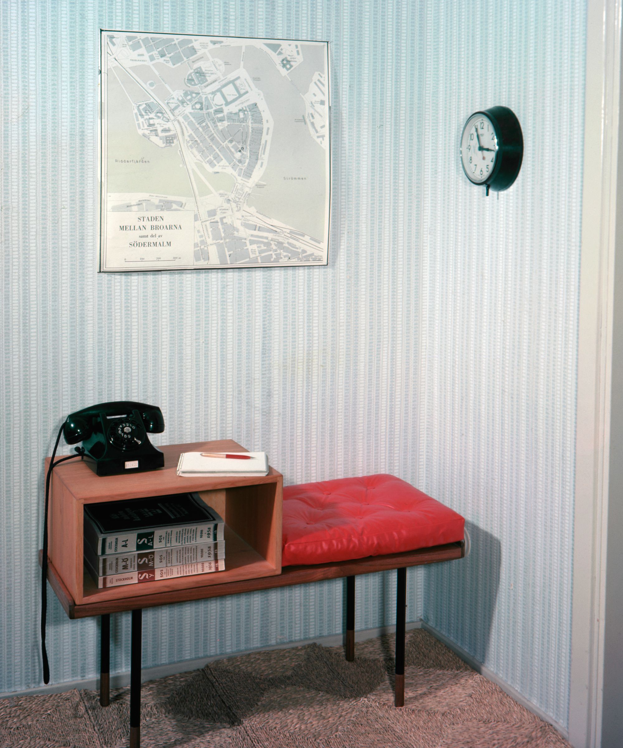 Hallway with striped pale blue wallpaper, midcentury wooden telephone bench with directory inside the shelf and a telephone on top, and a vintage map print above the bench on the wall