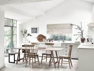 A white kitchen with distinct scandi feel by Neptune with wooden dining table in center and blind window treatment