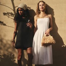 two models wear dresses one wears a black linen shift and the other wears a white dress with more volume in the skirt while posing 