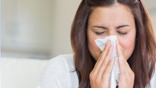 Woman sneezing into a tissue