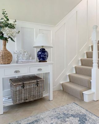 White hallway with table, jute runner stairs and white paneling on neutral walls