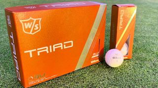 Wilson Triad Golf Ball in its orange packaging resting on the green