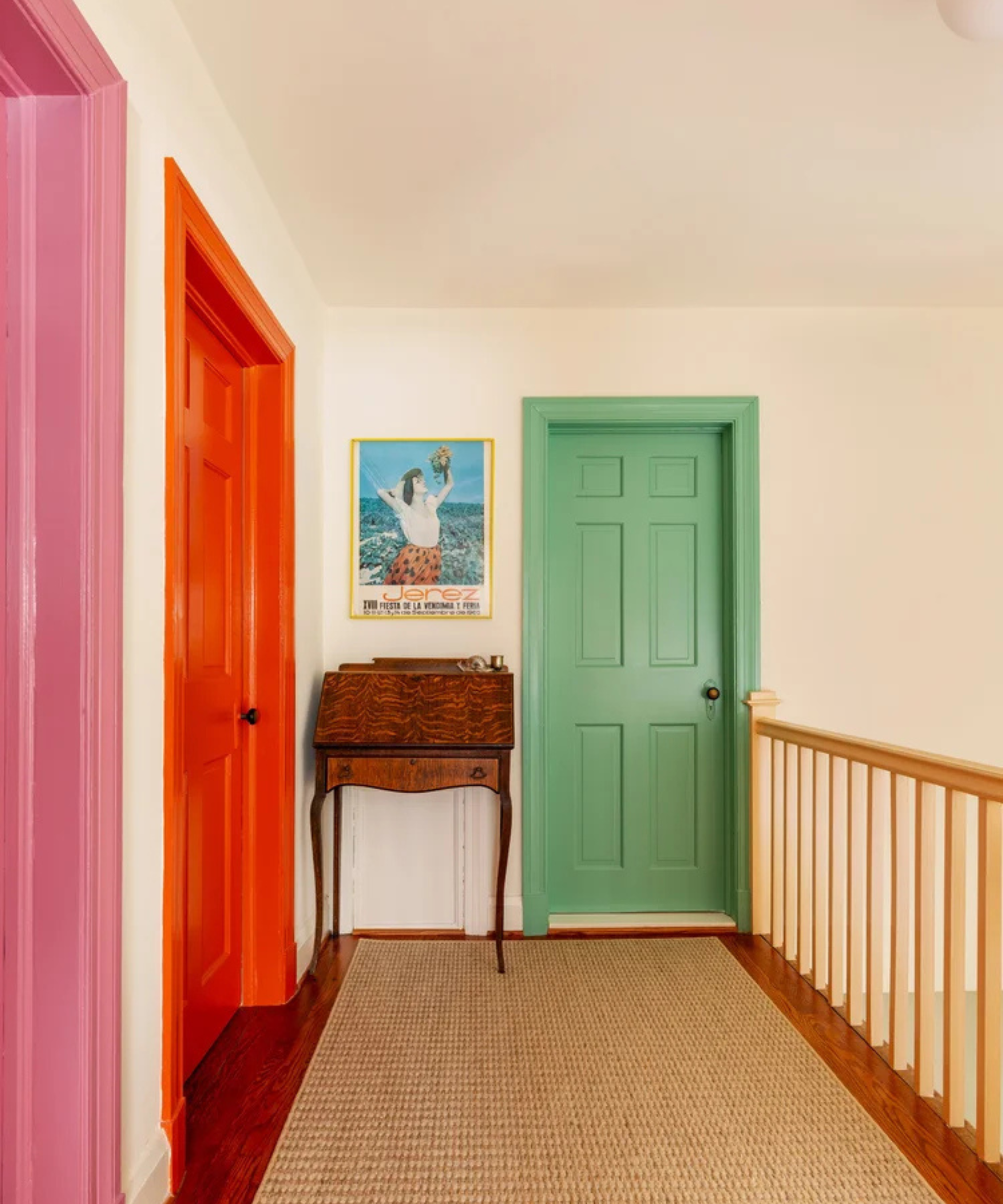 a hallway with three doors in pink, orange, and green, and a jute rug on the floor
