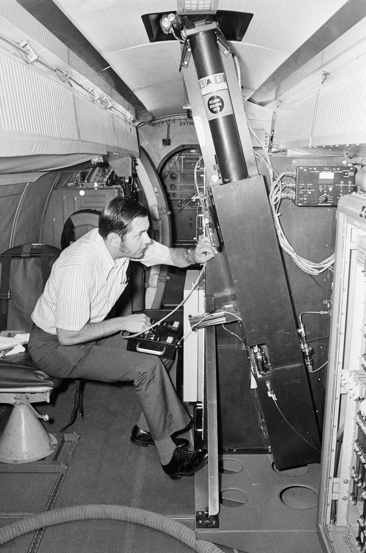 a man examines scientific equipment inside a cramped aircraft