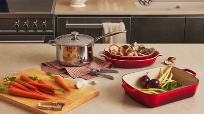 A Le Creuset red roaste, pie dishes, and stainless steel saucepan on a kitchen counter, ready to cook a fall meal