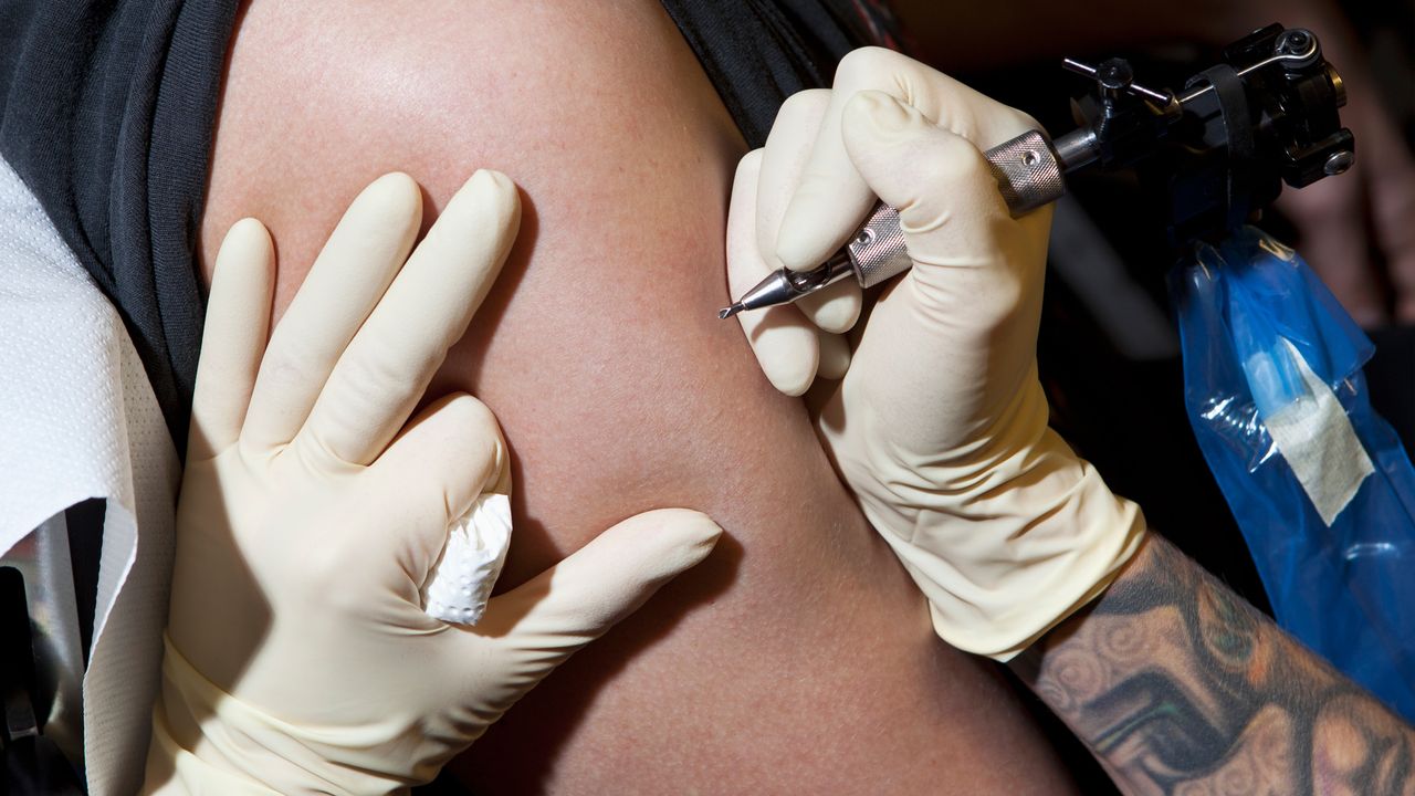 A tattoo artist prepares to tattoo an arm.