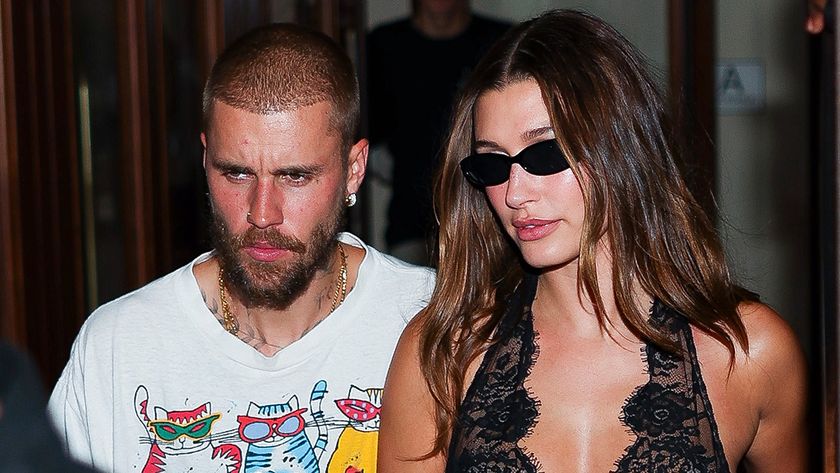 Justin and Hailey Bieber in New York City walking down the street. She has on sunglasses and a black satin gown and he's wearing a graphic tee with cats on it. 