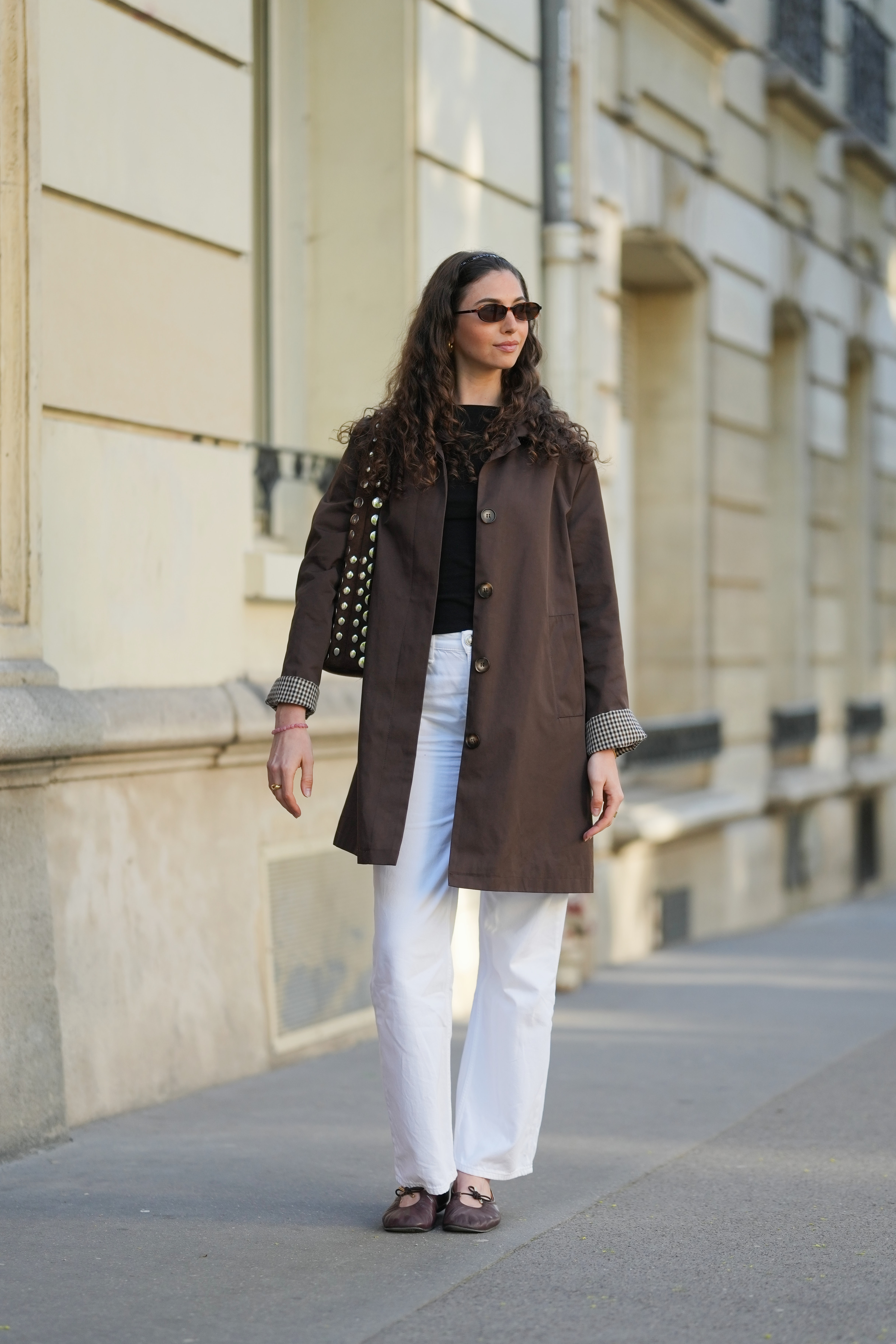 a woman wearing a brown jacket and white jeans