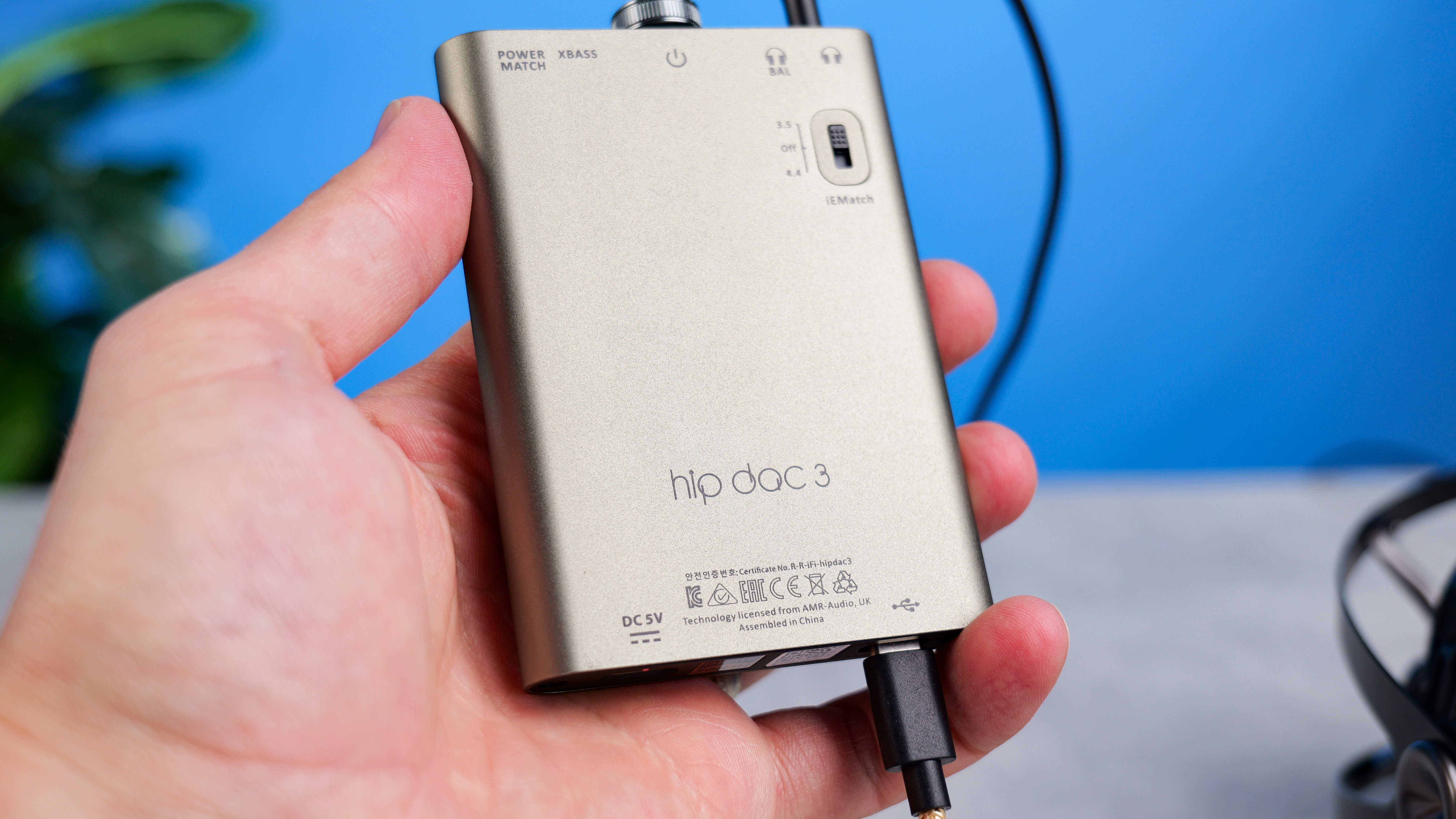 The iFi hip dac 3 in a person's hand with a blue background