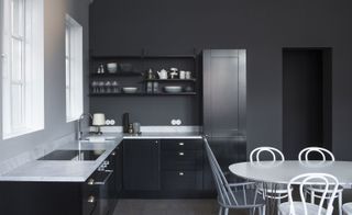 small kitchenette with dark wall and cupboards, white work surface and white table and chairs