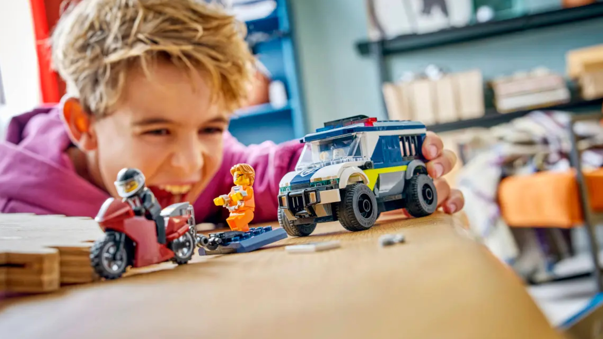 A child smiles while playing with the Lego Police Prisoner Transport Van on a wooden table