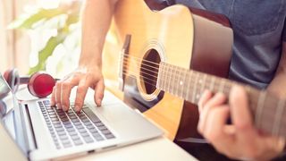 Musician playing acoustic guitar and learning from online lesson on computer