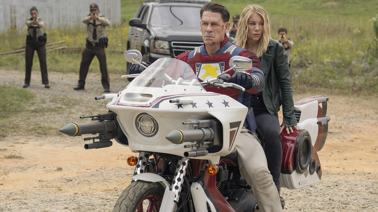 Chris Smith and Emilia Harcourt sitting on the Peace-Cycle while surrounded by cops in Peacemaker season 2 episode 7