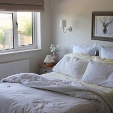 Ruffled bed with yellow bed sheets mixed with white pillowcases that have a thin blue stripe and a white wall light above the wooden side table
