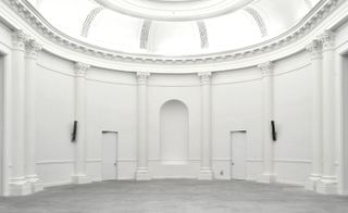 Interior view of Liège’s Fine Arts Museum featuring white curved walls, wall columns, a recessed arch in the wall, white doors and grey floors