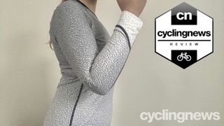 A close up side view of the reviewer's torso, wearing the black and white spotted base layer. Her arm is bent and raised, displaying the tightness of the sleeve around the elbow. A black and white 'Cyclingnews Review' badge is overlaid on the right