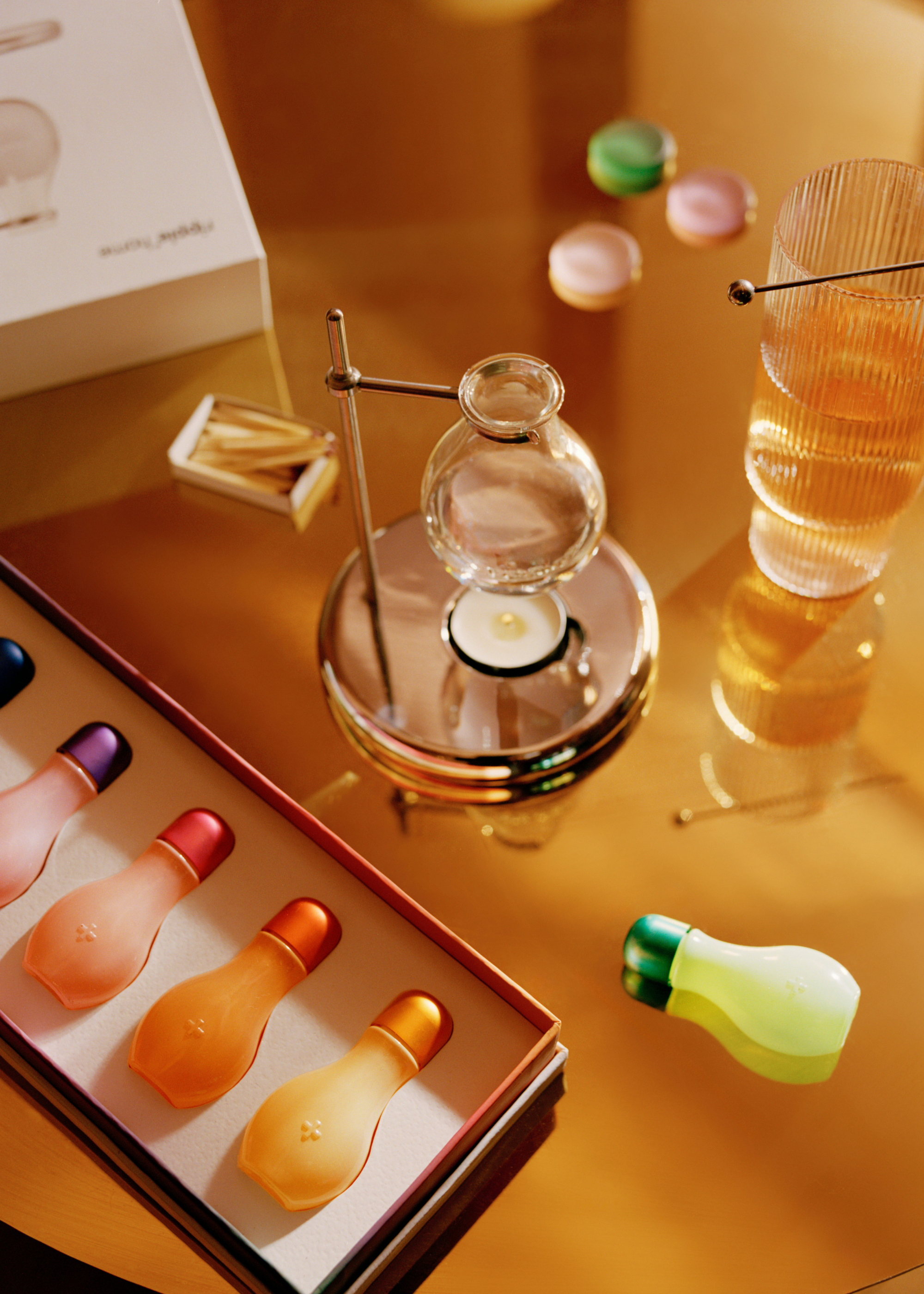 A chrome oil burner on a glass coffee table by a cocktail glass with a pick and a box of essential oils