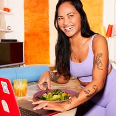 Young woman in purple gym gear with salad and lapttop in front of her