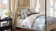 Cream bedframe with blue toile bedding and cream and white striped sheets