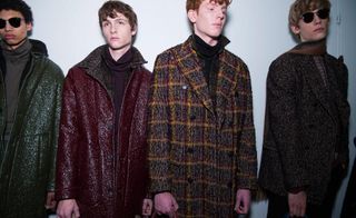 4 male models in long coats stand in a studio