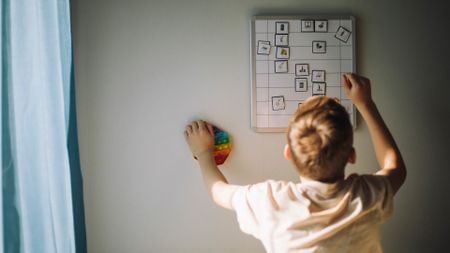 A boy with blond hair reaches up to fix a weekly calendar.
