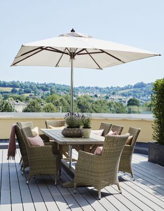 Wooden garden table with wicker chairs and white umbrella