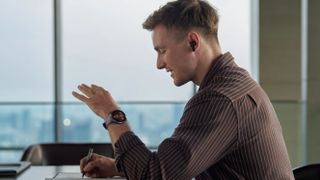 A man in an office with a Huawei watch on his wrist talking into his earbuds