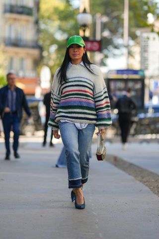 woman in oversized striped sweater, button dowh shirt, jeans, a green hat, and blue heels