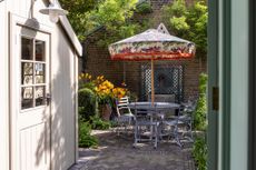 Small garden courtyard with garden mirror, outdoor table and parasol by Butter Wakefield
