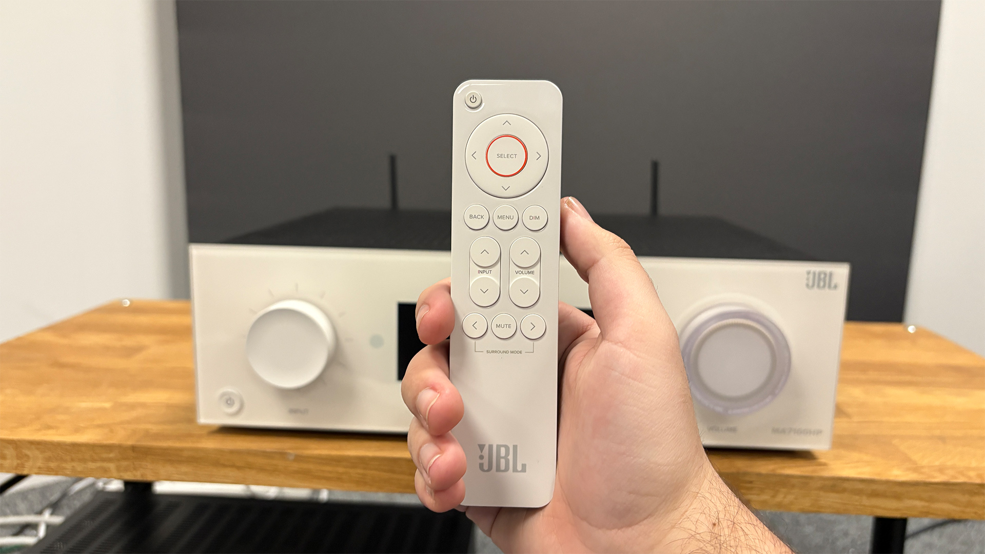 JBL MA7100HP AV receiver with remote control held in hand in front of it
