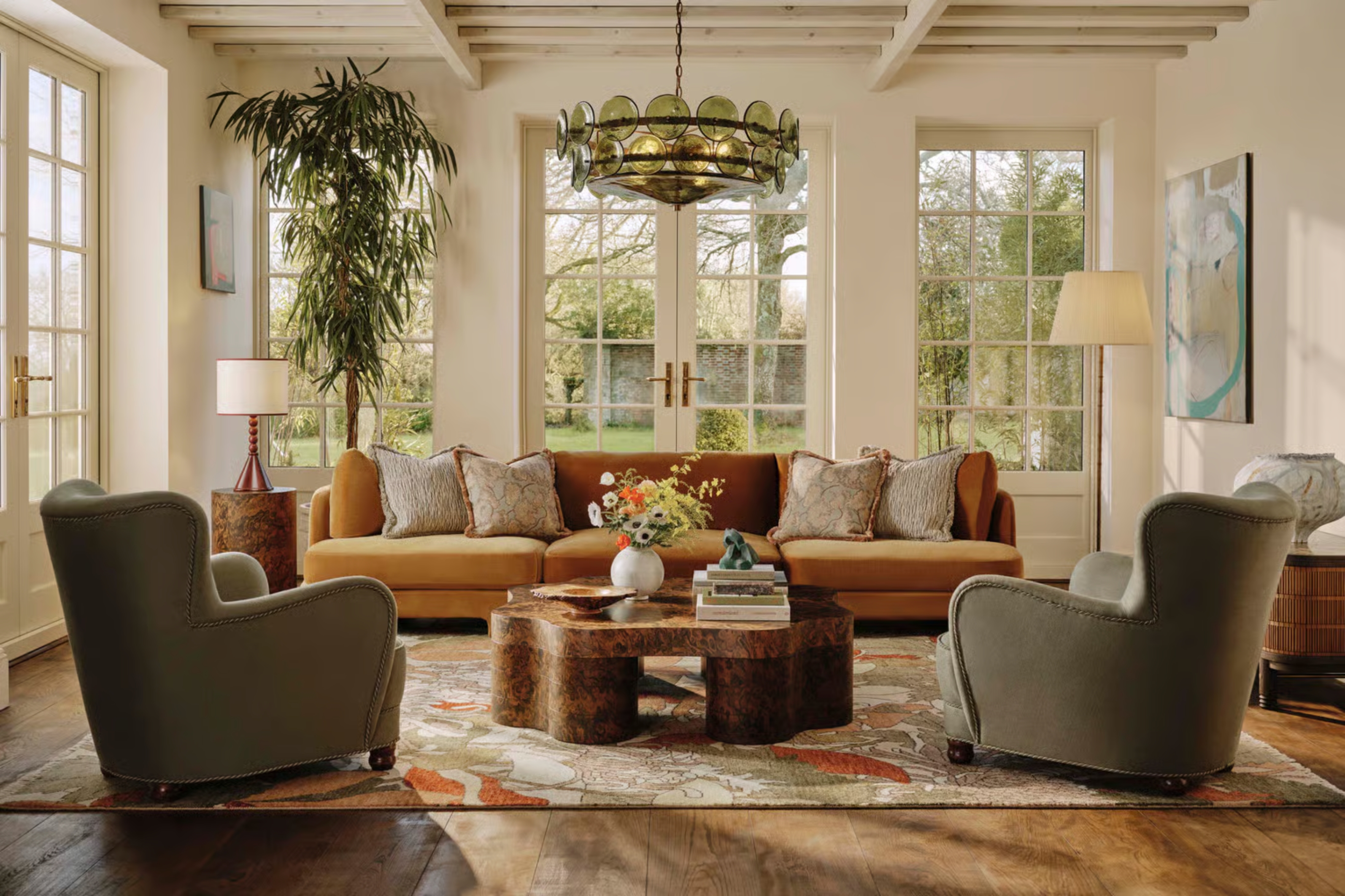 a living room in a light airy space with a sofa, two armchairs, coffee table, and green glass chandelier