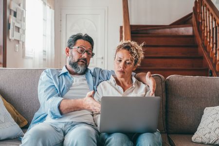Shocked couple looking at laptop screen frustrated by unexpected bad news online. 