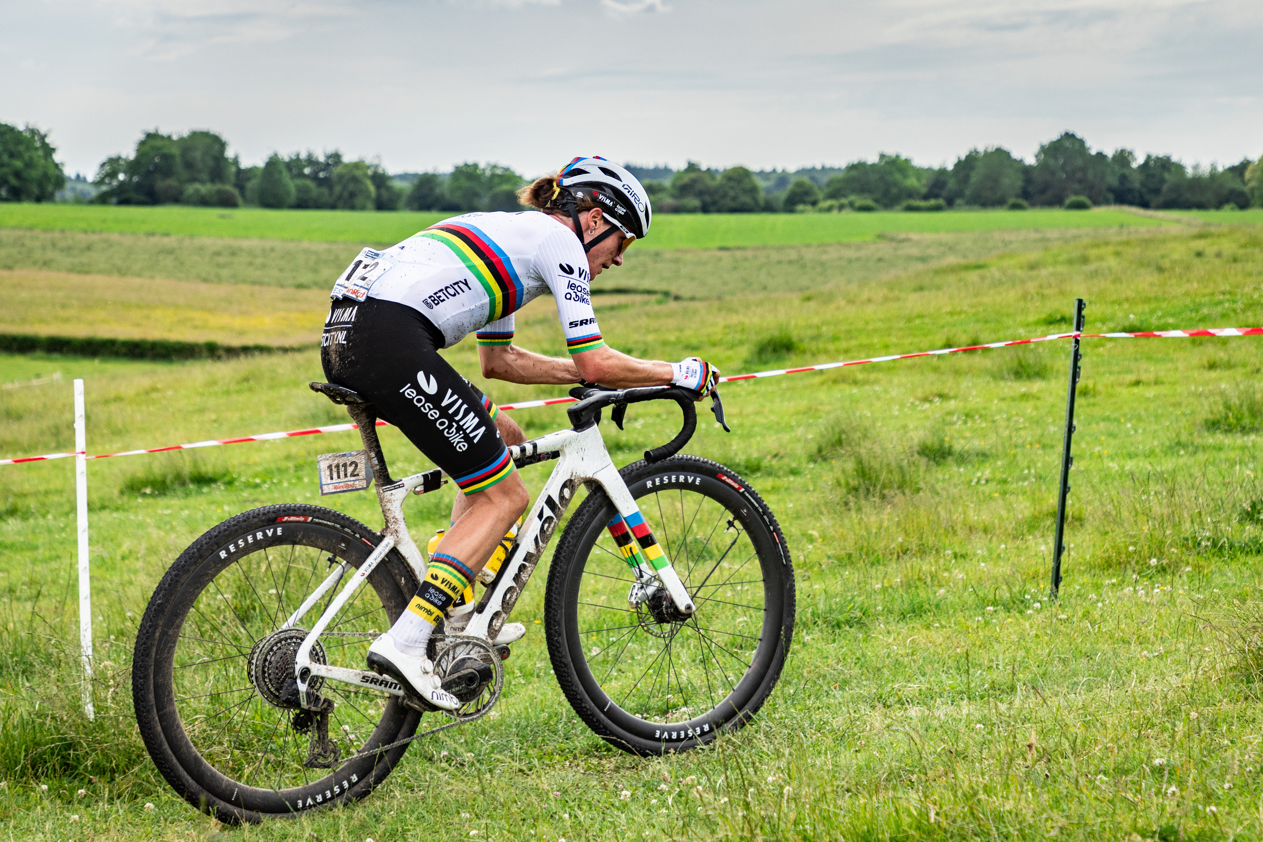 Marianne Vos riding a Cervelo Gravel bike up a shallow hill, in green fields.