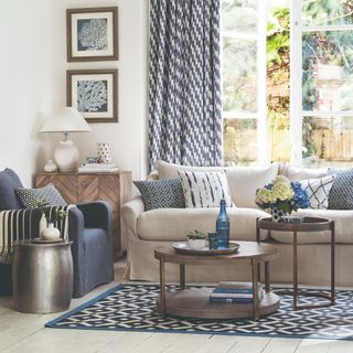 A living room with beige skirted sofa and a navy blue skirted chair around a complementing patterned rug