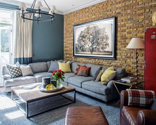 A living room with grey corner sofa, blue paint and exposed brick walls
