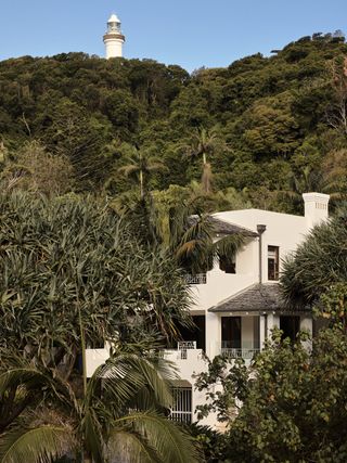 The white exterior of Raes guesthouses among the green coastal setting with Byron Bay lighthouse in the background