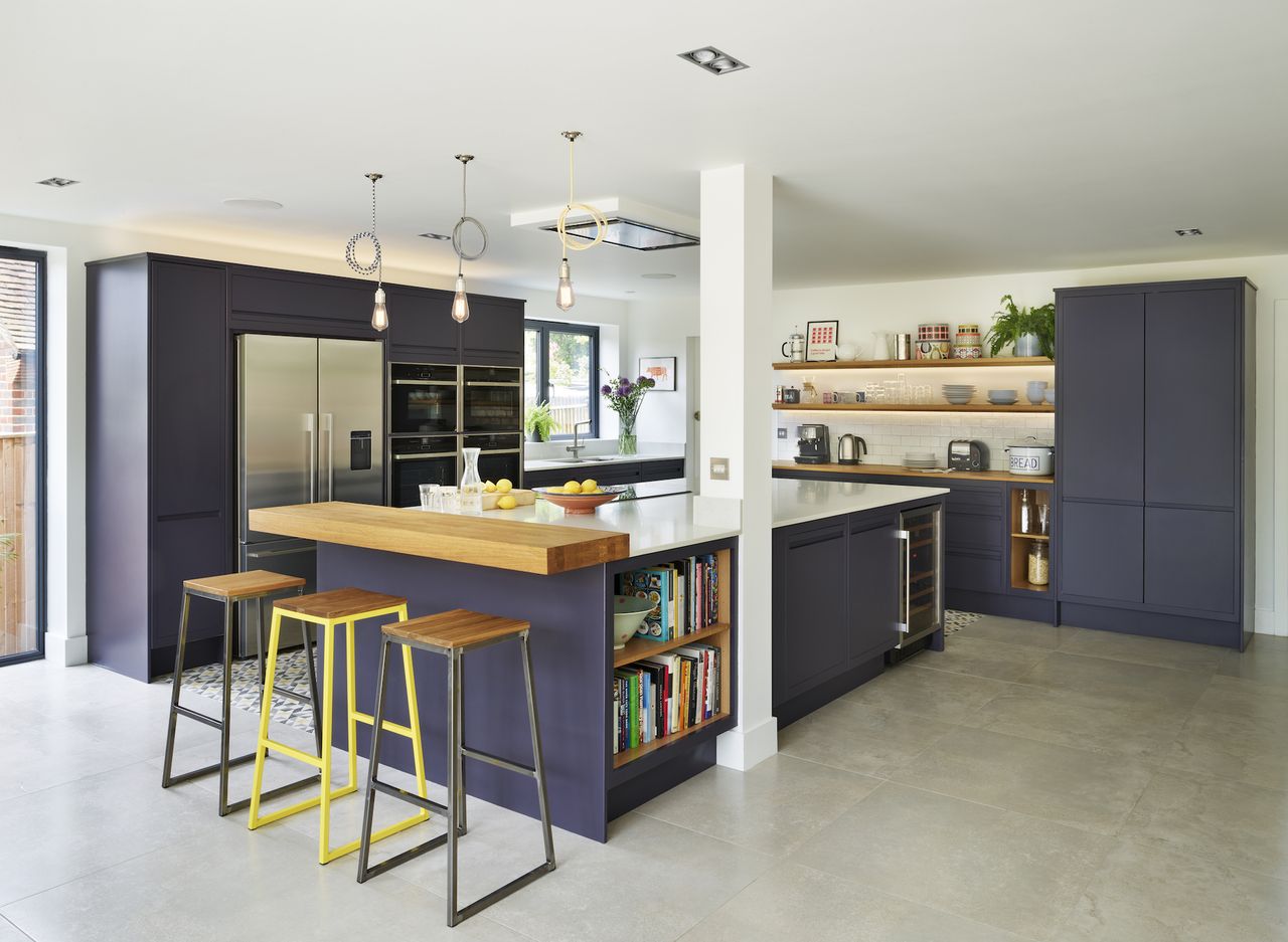 purple kitchen with kitchen island, open wood shelving and wooden breakfast bar, bar stools, stone floor