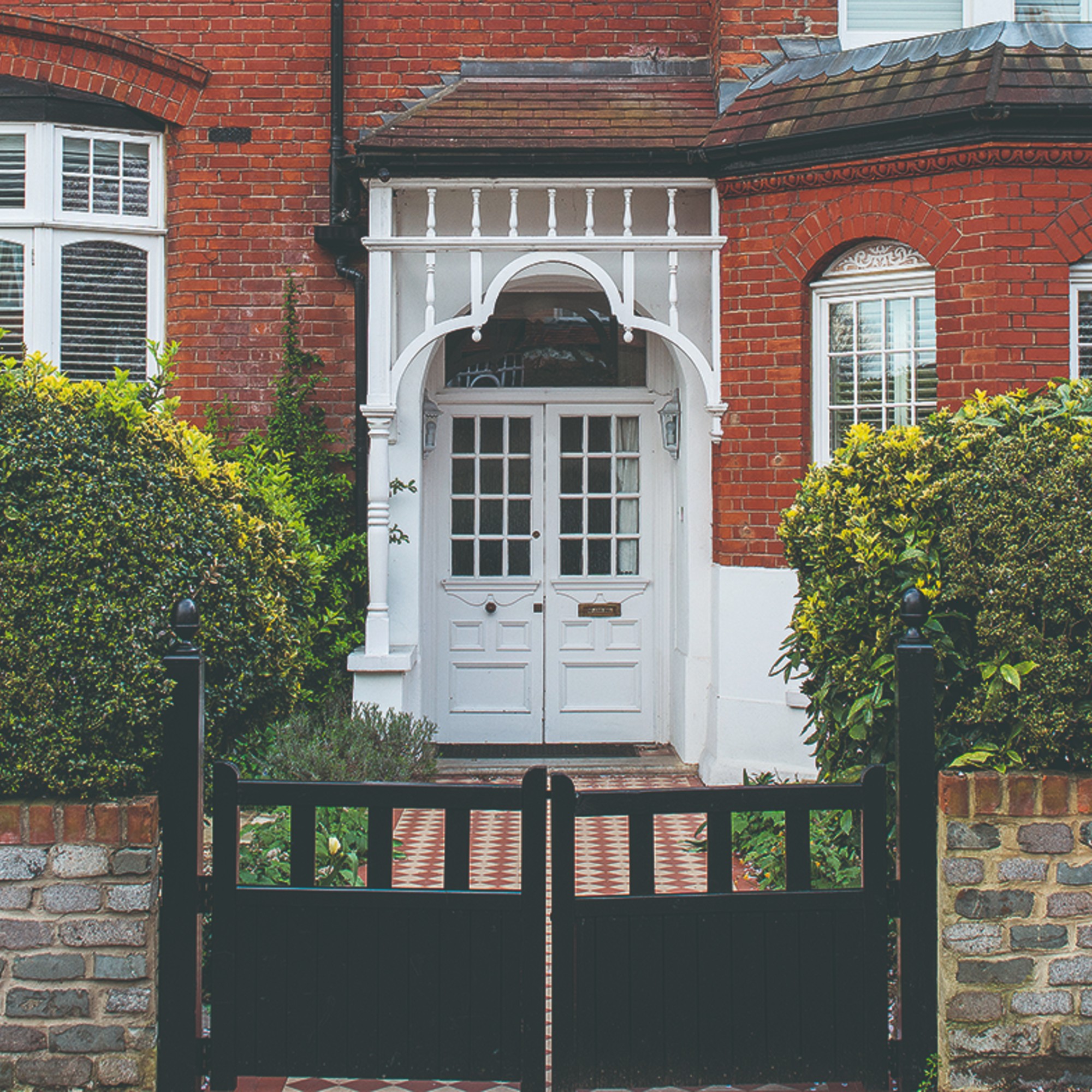 A red brick family home with a white double front door and a clear tiled pathway leading from the black front gate