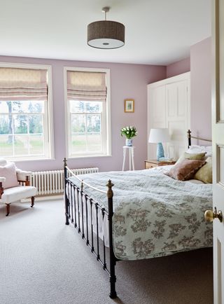 bedroom with pink walls and iron bedstead with nursing chair and Georgian sash windows