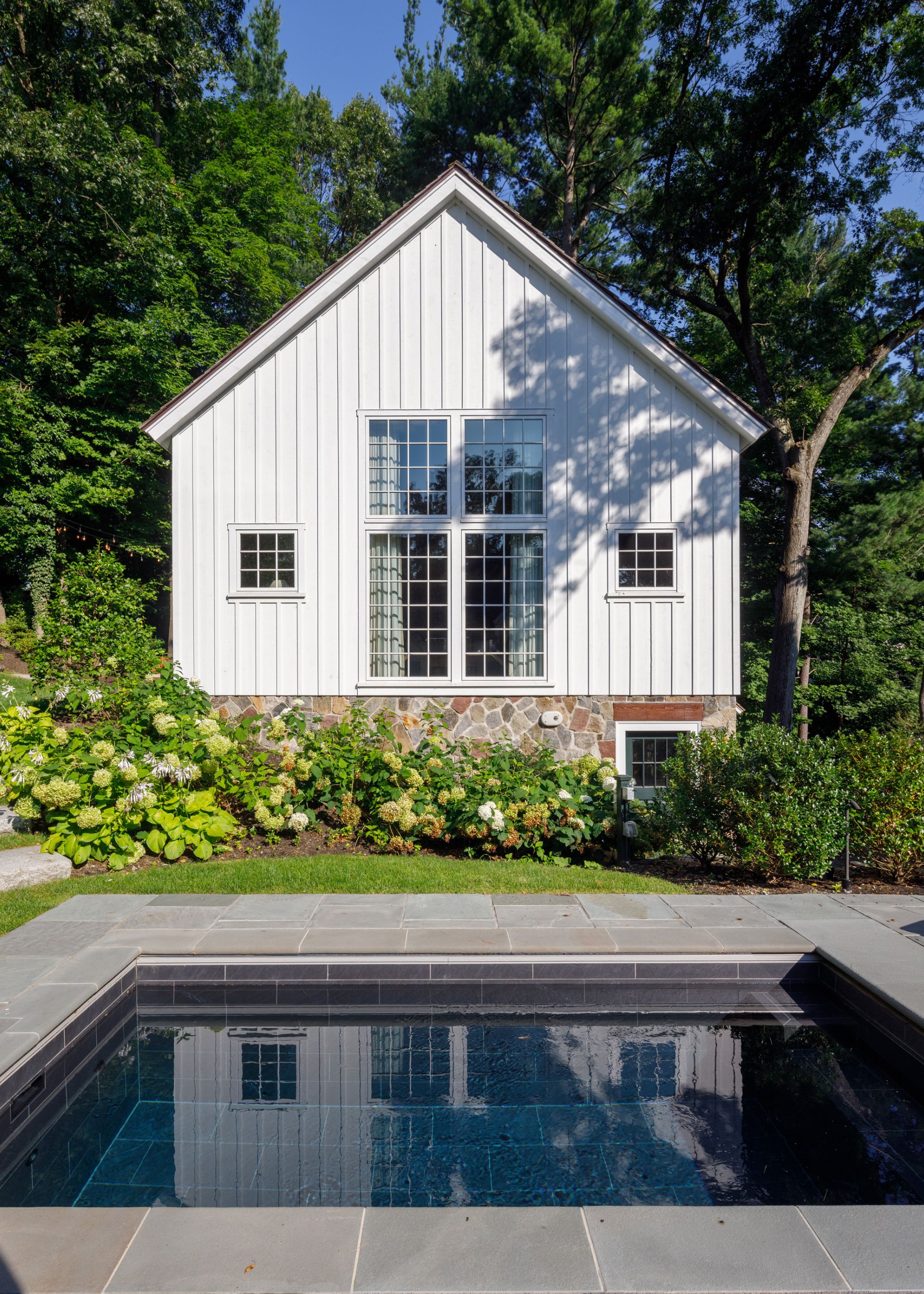 A small plunge pool outside of a home in a backyard. The backyard is filled with lots of plants and trees.